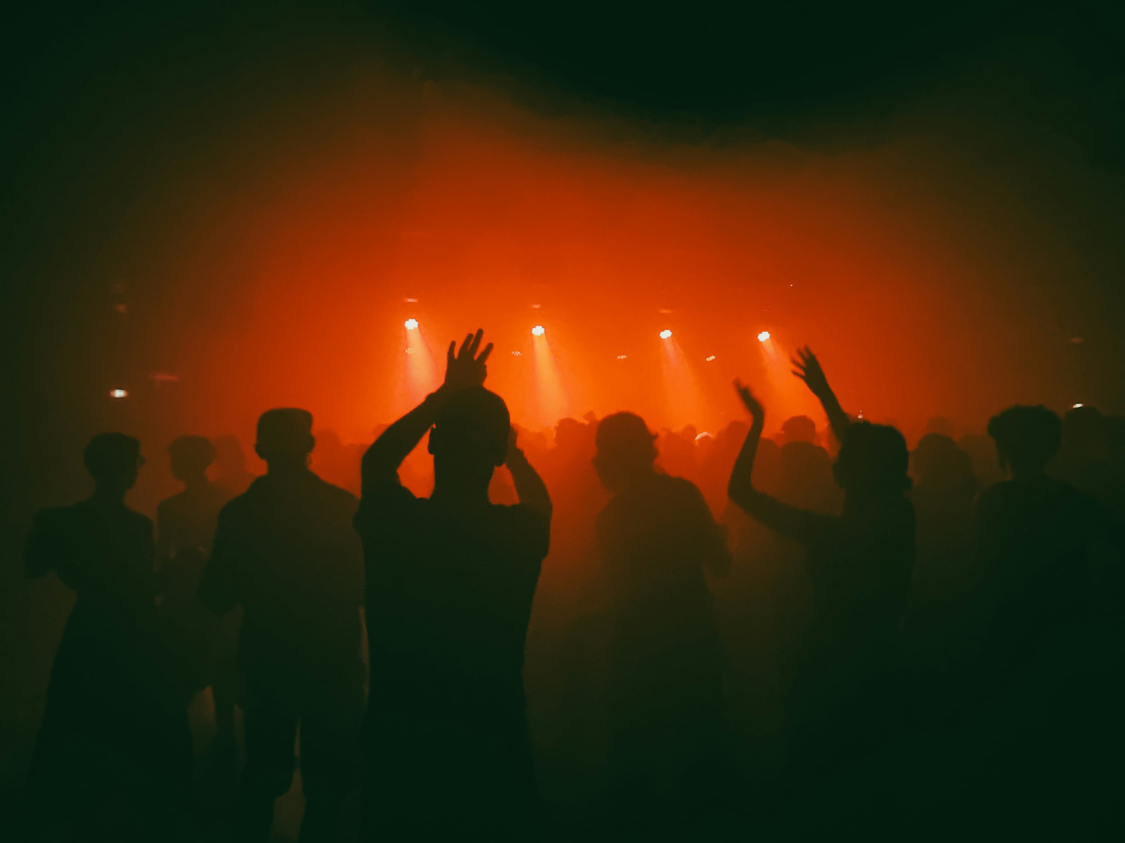 Crowd cheering at a packed live concert with red stage lighting