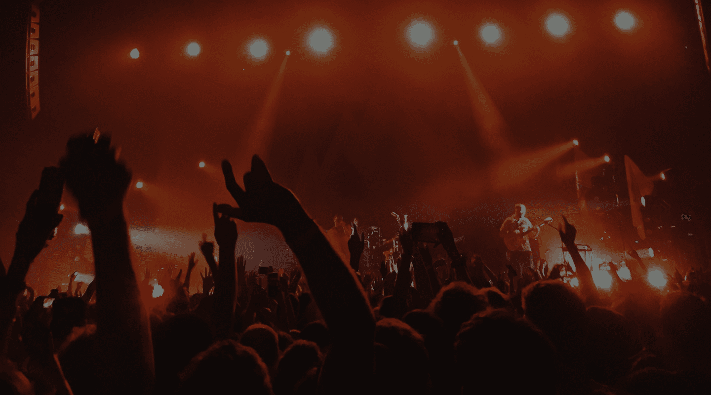 Crowd cheering at a packed live concert with red stage lighting